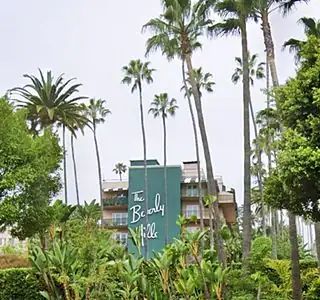 aquamarine facade reads The BEVERLY HILL, white letters, to the sidespalm trees
