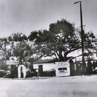 The Derby restaurant c.1940s Arcadia US66 black and white photo, 1940s, Derby restaurant sign to the left, trees around a building, cars parked left. Street in front