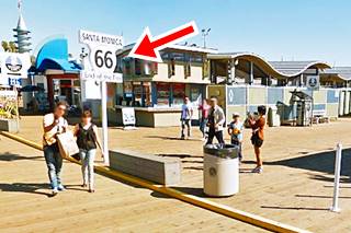 End of Route 66 sign on Santa Monica Pier people on the boardwalk with the End of Route 66 sign, and stalls and shops