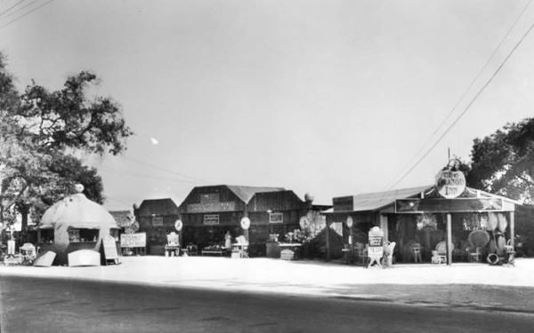 Orange Inn 1927, Arcadia CA Route 66 black and white 1927. Route 66 runs left to right. Long narrow building single story, wood, with large orange to the left, a stand selling juice. Sign to the right reads THE ORANGE INN