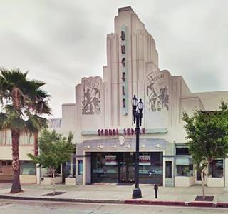 art deco building with tower in middle of facade, palm trees, street in front