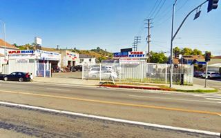 corner former gas station, service bays left, building right, single story flat roofed, now muffler shop. White fence.