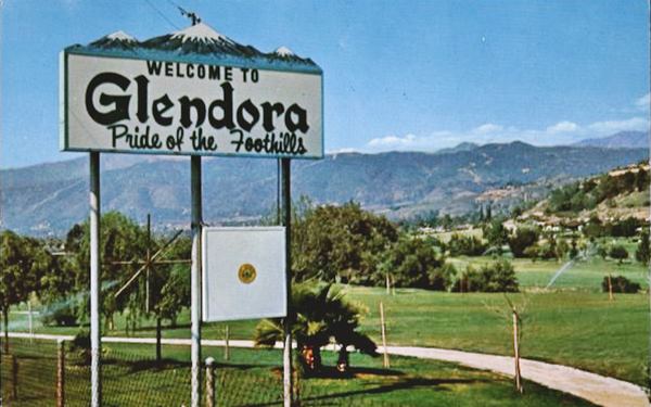 sign by the side of the highway in a golf course. Mountains in the distance. It reads WELCOME TO GLENDORA, PRIDE OF THE FOOTHILLS, with a depiction of a snow capped mountain