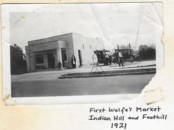black and white, 1921 box shaped building, people, cars text reads: FIRST WOLFE’s MARKET INDIAN HILL AND FOOTHILL 1921