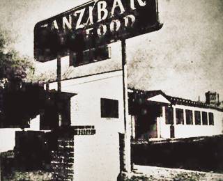 Zanzibar Cafe opening 1945. Duarte CA black and white photo in newspaper with a gable roof building and sign reading ZANZIBAR seafood