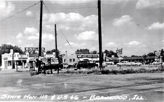 black and white 1950s, cars, on US66 seen from the railroad. Gas station, cafe and motel line up beyond the road