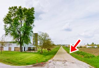 narrow concrete road runs by a farm, and fields