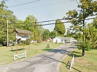 Sign, and beyond it a lawn and driveway, and the main gable roof motel building with trees around it