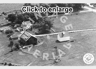 Meramec Barn 1966 Lexington IL Black and white, 1966, aerial view buildings, roads, trees and a barn with MERAMEC CAVERNS written on its roof