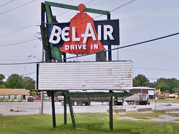 old neon sign in a field, words BELAIR Drive In written a red bell, vintage white marquee below and a green arrow