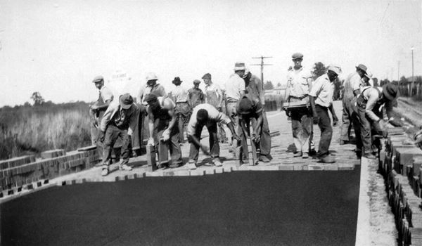 black and white photo of men, with bricks and a tar coated roadbed