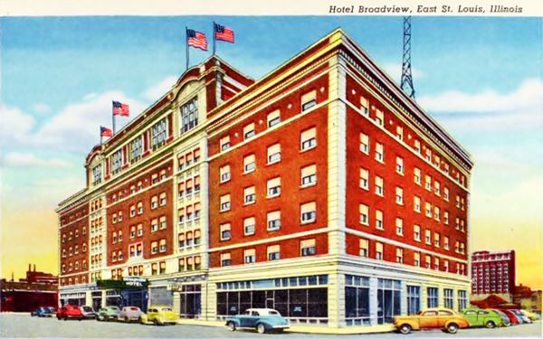 color postcard c.1940s of a six story red-brick hotel with cars parked and US flags flying