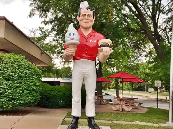 muffler man with cap, holding a burger and an ice cream, red shirt