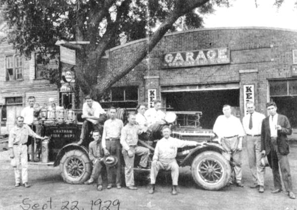 black and white photo of men on a fire truck, dated 1929, in front of a brick garage, arched facade sevice bay in the middle