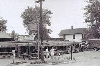black and white c.1950, man and woman on a corner grocery shop, truck and signs say Casey Grocery Basket