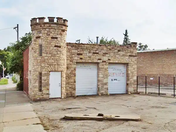 castle shaped sandstone building, turret, 2 service bays with white shutters, concrete gs pumps island