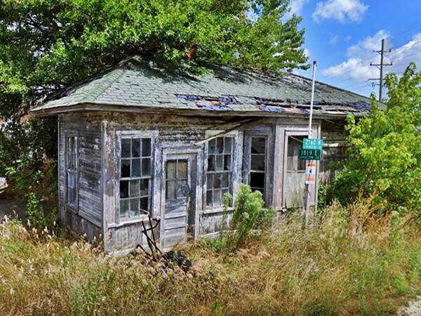 decaying woodframe building with weeds and trees around it