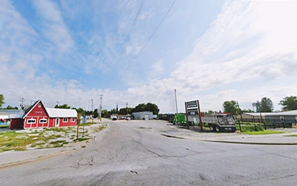 color, 2023: crossroads with building on the left, gravel parking area right. Church in the distance