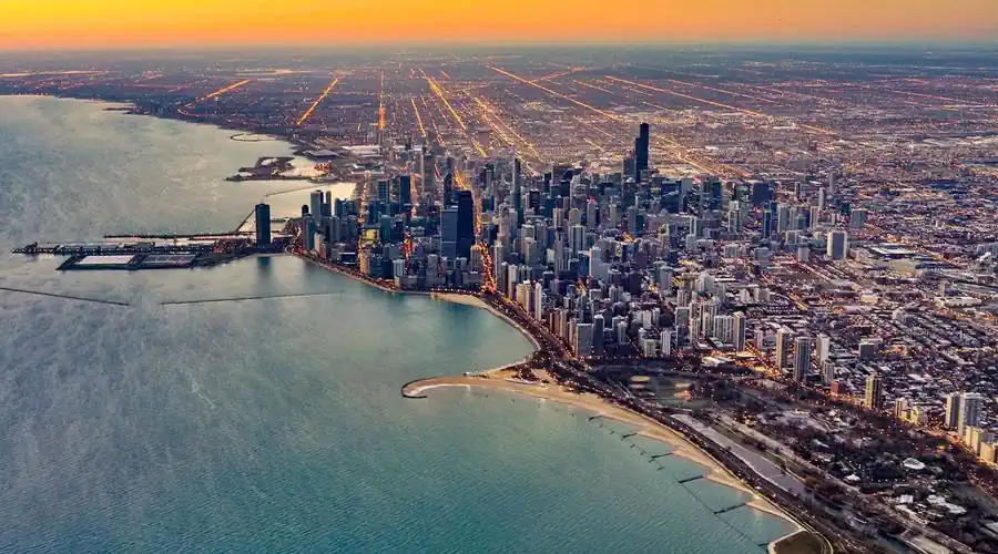 air view of Chicago, skyscrapers, streets, lit up at sunrise, Lake Michigan (left), pink-red-yellow sky