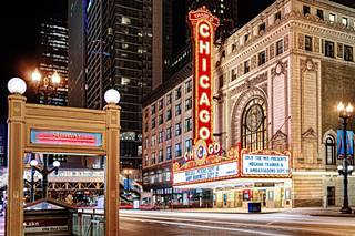 Chicago Theater color, marquee with vertical neon sign says Chicago Theater, at night, lit up, classic sandstone building 7 stories high, stree in front