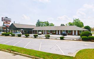 hip roof building, a motel seen from the highway, long, single story, neon sign to the left