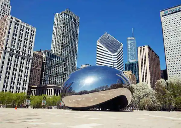 A large, highly-polished, mirrored bean-shaped sculpture with skyscrapers beyond