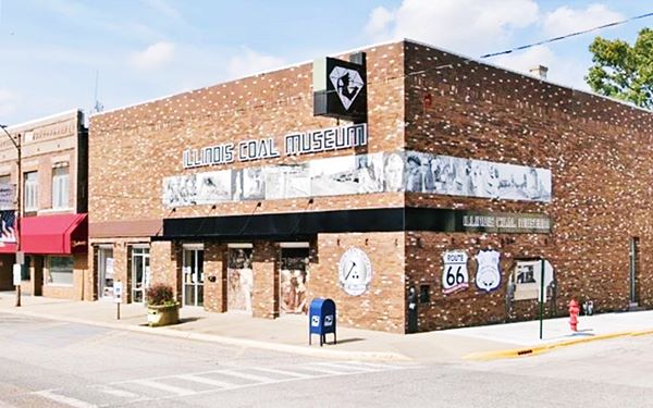 corner building with murals, one of them a Route 66 shield, on its south facade, a museum facing main street