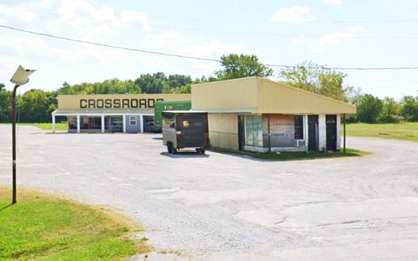 vacant boarded Amoco station with modified roof, and beyond it a old Restaurant with the word CROSSROADS on its yellow facades
