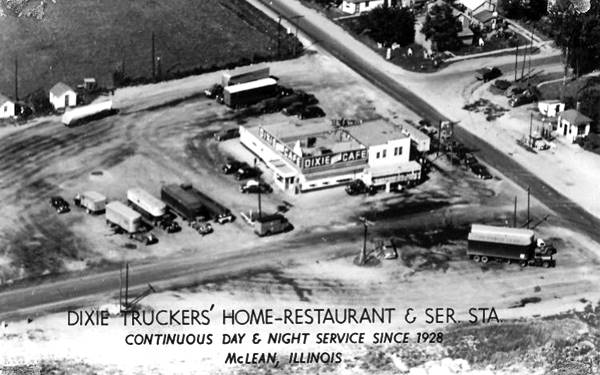 black and white aerial photo truck stop, trucks, US66 cuts across image uper right, houses, trees