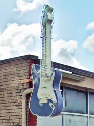 sign on a corner, shaped like an electric guitar, pale blue and white, neon lights