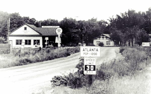 black and white, 1930s, narrow curving US66, hip roof building with Texaco sign and canopy to the left. Trees, Atlanta city limits sign