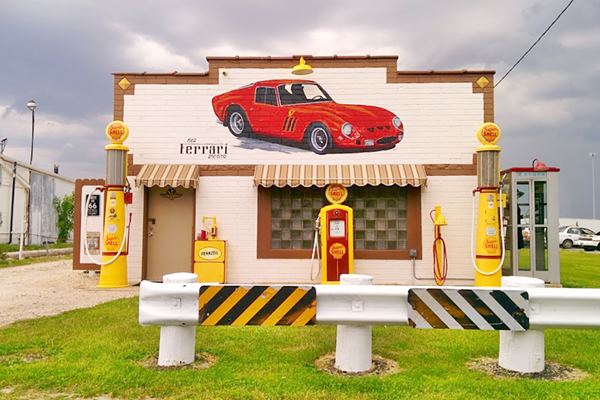 replica of a gas station with red car painted mural on facade and yellow vintage Shell gas pumps