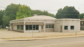 color, single story, with garage service bays and large windows for displaying vehicles; a semi domed roof crowns the building