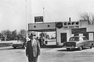 1954 Fern’s Cafe Black and white 1954. Man in suit, with hat standing by Cafe with gas pumps, cars, and beyond the highway