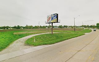 site of Gas for Less Benld IL field with a sign by a highway and a white curved driveway