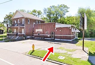 gable roof two story house next to flat box-shaped brick gas station with pump island visible