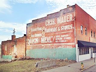 white letters on a red brick wall of a two story building advertising stoves and hardware for cooking