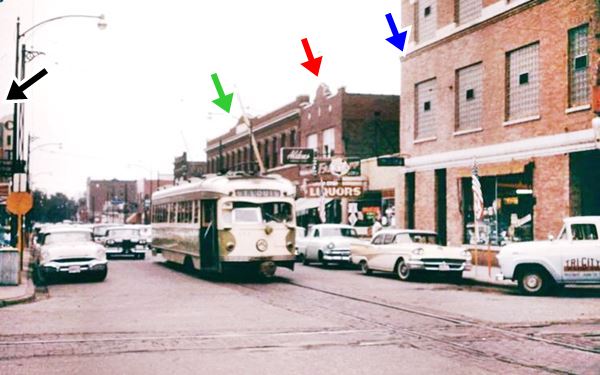 color photo of a busy street in 1958 with a streetcar, red-brick buildings, vintage cars parked in Granite City