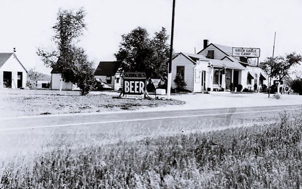 black and white photo c1930s of a gable roofed, long, single floor building facing highway, 1930s jalopy, sign saying "Beer" and "Green Gable Camp"