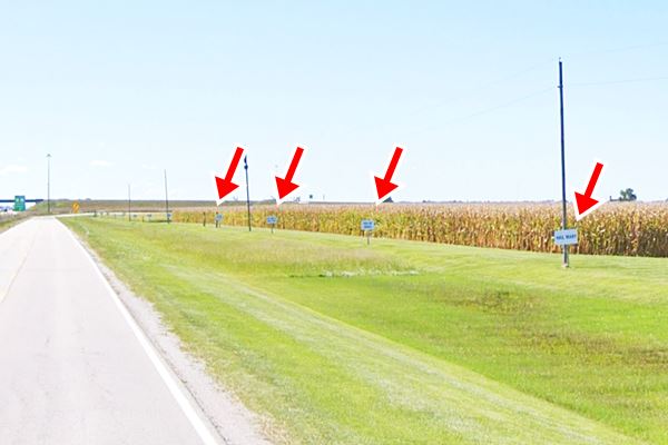 signs spaced along the side of a corn field facing US66 with blue letters on white background with the Hail Mary prayer