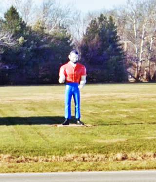 field, trees in the background, muffler man with orange shirt and jeans