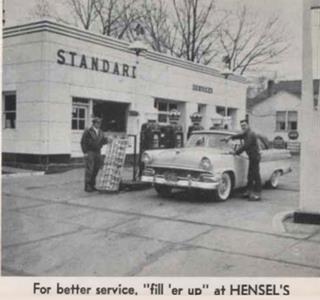 Hensels Standard Station on US 66, Plainfield, 1958 Black and white, 1958 two men by a car at a Standard gas station with 4 pumps, office behind them