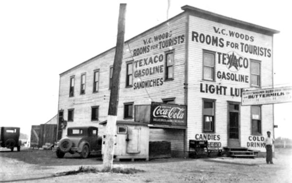 1930s Hide-A-Way tavern black and white 1930s narrow 2 story building with advertising on it (rooms for tourists, Texaco Gas, buttermilk, cold drinks, candies etc) vintage cars and man