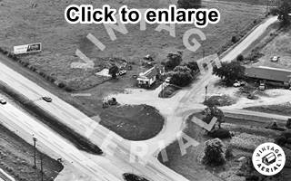 aerial view of Hill Top Cafe and US 66, 1972 Black and white, 1972, aerial view of 4-lane US 66 and top, a road crossing it with a gable roof building on the upper left corner, houses and trees