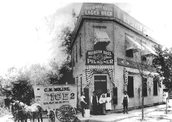 1870s black and white triangular corner building, woodframe 2 stories, people, horse and cart, Hofmann beer lager signs.