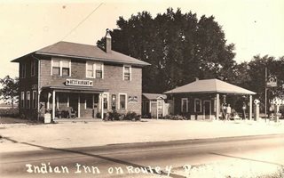 sepia, 1930s, 2 story hip roof INDIAN INN, and (right) hip roof gas station with pumps and sign, US 66 runs in front of both