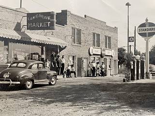 Lake Drive Market on US66 c.1950s black and white, 1950s. Brick buildings with a market, cafe, Standard gas station, people on the sidewalk, gas pumps and cars