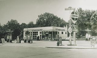 Lambert gas station c.1957 ALT66 Joliet Black and white, 1957 gas station, Standard Oil, sign, cars pumps, trees behind, box shaped, no canopy, on a corner, seen from ALT US66