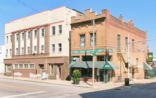 red brick corner building 2 stories, a grill, to its left 3 story former theater bldg.