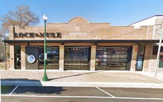 red brick single story stepped parapet building with stone inset in the middle, large windows, former car dealership, now a restaurant